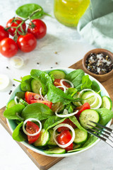 Diet menu. Healthy vegetable salad of fresh tomato, cucumber, onion and spinach on slate, stone or concrete background.
