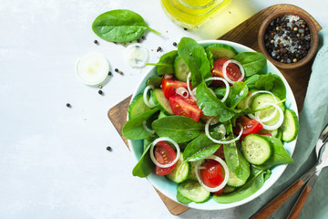 Diet menu. Healthy vegetable salad of fresh tomato, cucumber, onion and spinach on slate, stone or concrete background. Top view flat lay background. Copy space.