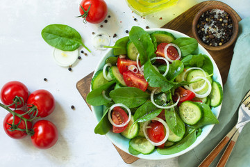 Diet menu. Healthy vegetable salad of fresh tomato, cucumber, onion and spinach on slate, stone or concrete background. Top view flat lay background.