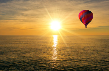 A hot air balloon over the sea at sunrise