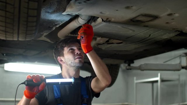 Mechanic with a flashlight repairs a car 