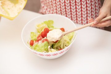 Cooking Salad. Female hands add the sauce to Caesar.