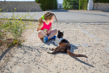 funny friends: little girl, five years old child sitting on the ground and white and black cat...