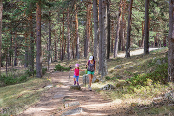 mountaineer family: mother and daughter, five years old girl, with caps and trekking sticks, hiking on trail in forest of Canencia (Madrid, Spain, Europe)
