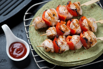 Closeup of grilled chicken skewers on green tortilla flatbread, selective focus, horizontal shot