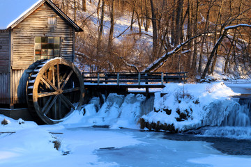 Rural landscape with old abandoned watermill in woods. Snowy winter view of obsolete wooden mill and waterfall between trees in sunlight. Travel America, Wisconsin, Midwest USA. © Maryna