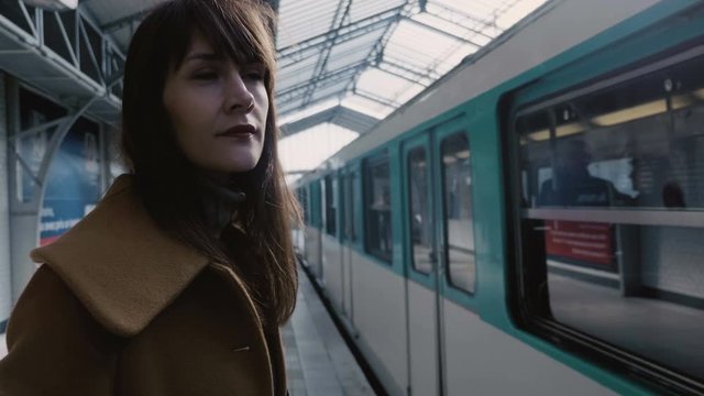 Young calm beautiful Caucasian business woman waiting for coming up metro train at Paris railway station slow motion.