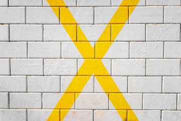 Large X shaped yellow cross painted on the pavement, background of a parking lot.