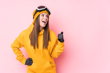 Young caucasian skier woman isolated points with thumb finger away, laughing and carefree.