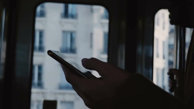 Dark cinematic close-up silhouette of female hands using smartphone at moving metro train door windows slow motion.