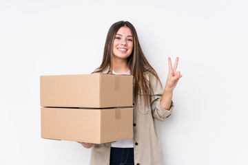 Young caucasian woman moving to a new home joyful and carefree showing a peace symbol with fingers.