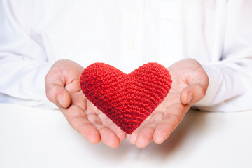 Red heart in the hands of a young Caucasian type man on a light background. Valentine's day concept. Copy space for your text.