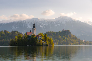 The Pilgrimage Church of the Assumption of Maria on the island on Lake Bled, Slovenia with the surroundings mountains and the Bled castle in the background, at dawn