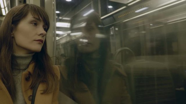 Portrait of young calm thoughtful beautiful Caucasian passenger woman looking out of metro train window slow motion.