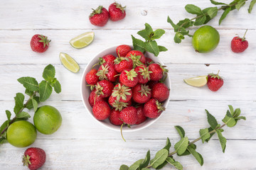 Bowl with strawberries. Fruits and berries on a white wooden table. Strawberry, mint, lime, mint. View from above. Top view. Free space for text.