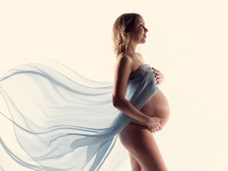 Pregnancy woman open tummy naked body skin. Photoshoot of a pregnant girl with flying blue cloth....