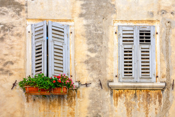 Fototapeta na wymiar Facade of an old dirty house with blue shutters and flowers in a flowerpot