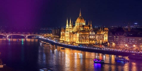 Obraz premium Colorful sunset over Budapest. Wonderful evening cityscape. Night view of the illuminated building of the Hungarian parliament over Danube river with reflected. Popular touristic locations