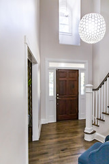 Interior Front Entrance Lobby of home with Vaulted cathedral ceilings and a window with a dark stained wood front door and globe shaped chandelier hanging light