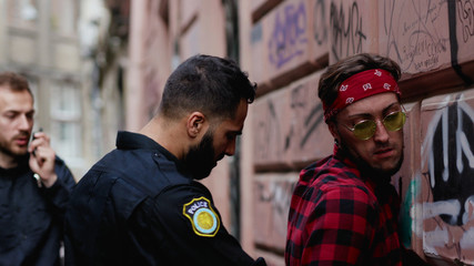 Fototapeta premium Police in the city. Close-up of strong severe policeman searches a drug dealer finds dangerous drugs handcuffs a criminal and leads him to the car. Arrest.