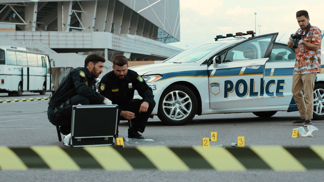 Police raid. Two police officers examine evidence in crime area. Criminological expert takes pictures on camera to provide detailed investigation.