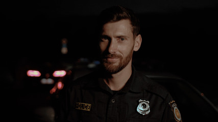 Zoom in portrait of attractive positive american cop smiling joyfully standing against police...