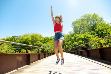 Happy and funny young woman jumping on a bridge in a sunny day