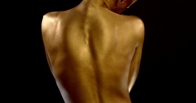 naked back of young woman covered golden paint, she is embarrassing and stroking herself