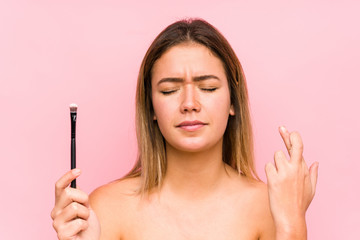 Obraz premium Young caucasian woman holding a eyebrush isolated crossing fingers for having luck
