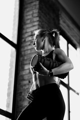 black and white beautiful young girl trainer stands near the window and holds in her hands a roll for warming up muscles in leggins. Loft gym in which the sun shines