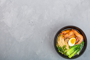 Asian noodle soup, ramen with shrimp, vegetables and egg in black bowl on gray concrete background. Flat lay, Top view, mockup, overhead. Healthy food concept