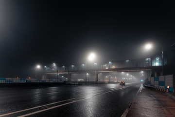 Foggy misty night road and overhead pedestrian bridge illuminated by street lights