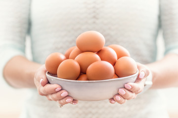 The hands of a young woman hold a bowl of chicken eggs