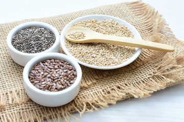 Quinoa, chia and linseed seeds on light wood background
