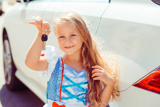 We got a new car. Child holds shows keys in right hand staying next to their new white car