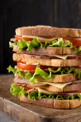 Delicious sandwich with ham, cheese, tomatoes, lettuce. High club sandwich with toast. close up of fresh sandwich with ham, bacon,tomatoes,cheese and lettuce On a wooden board. Sandwich bread tomato, 
