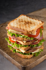 Delicious sandwich with ham, cheese, tomatoes, lettuce. High club sandwich with toast. close up of fresh sandwich with ham, bacon,tomatoes,cheese and lettuce On a wooden board. Sandwich bread tomato, 