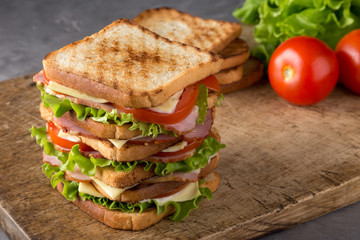 Delicious sandwich with ham, cheese, tomatoes, lettuce. High club sandwich with toast. close up of fresh sandwich with ham, bacon,tomatoes,cheese and lettuce On a wooden board. Sandwich bread tomato, 