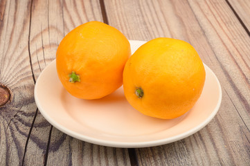 Two ripe yellow lemons on a white plate on a wooden background. Close up.