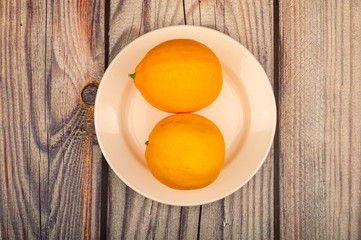 Two ripe yellow lemons on a white plate on a wooden background. Close up.