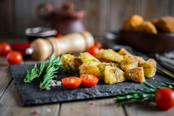 Spicy potatoes baked in the oven on a gray dish with herbs and tomatoes on a wooden table