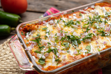 Mexican red baked enchiladas with melted cheese and sour cream on wooden background