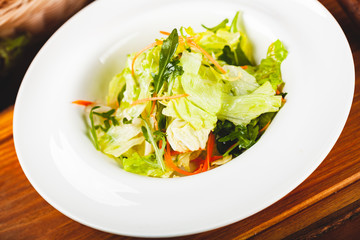 Fresh mixed green salad with carrot on white plate.