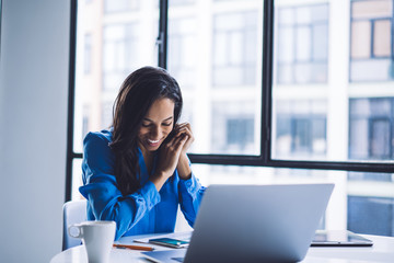 Pleased black businesswoman reading message on smartphone while sitting at office table
