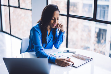 Concentrated black woman working touching screen of tablet at table