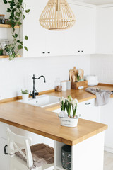 Modern white u-shaped kitchen in scandinavian style. Spring decoration spring flowers