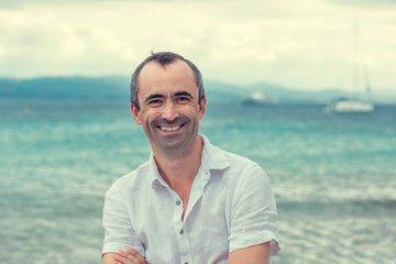 Smiling man with crossed arms by the sea, toothy smile middle ag