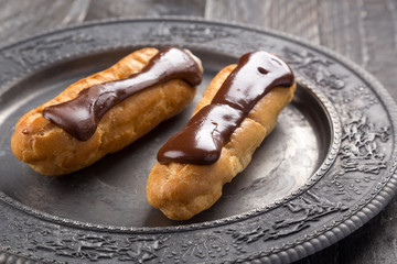 Tasty eclairs on a plate on a white wooden table. Served with flowers. Rectangular gray plate. Traditional french eclairs with chocolate. Home made cake eclairs. Traditional eclairs, profitroles class