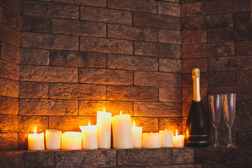 Two glass glasses with a champagne bottle near a stone wall with the burning candles