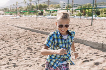 Portrait of happy cute white kid running cheerfully outdoor on sunny beach of hotel resort during summer vacations.